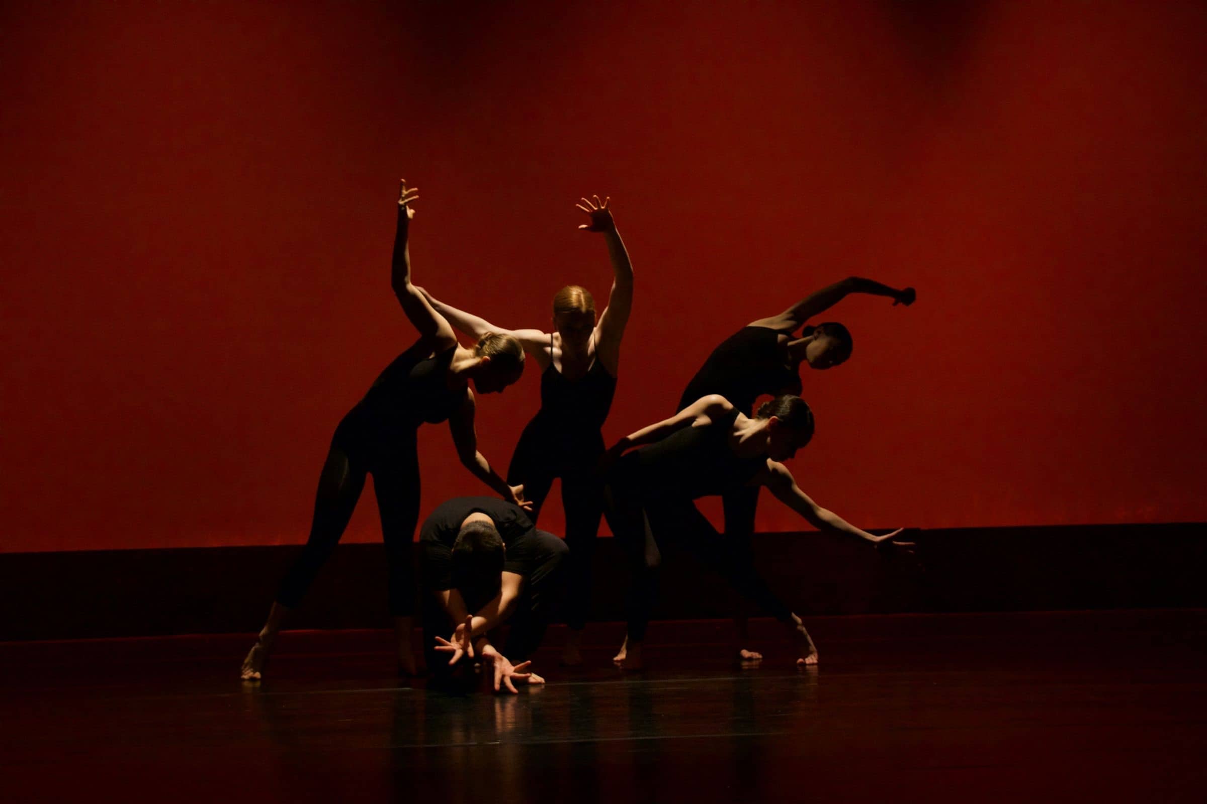 Grupo de bailarines en una figura conjunta sobre un fondo rojo.