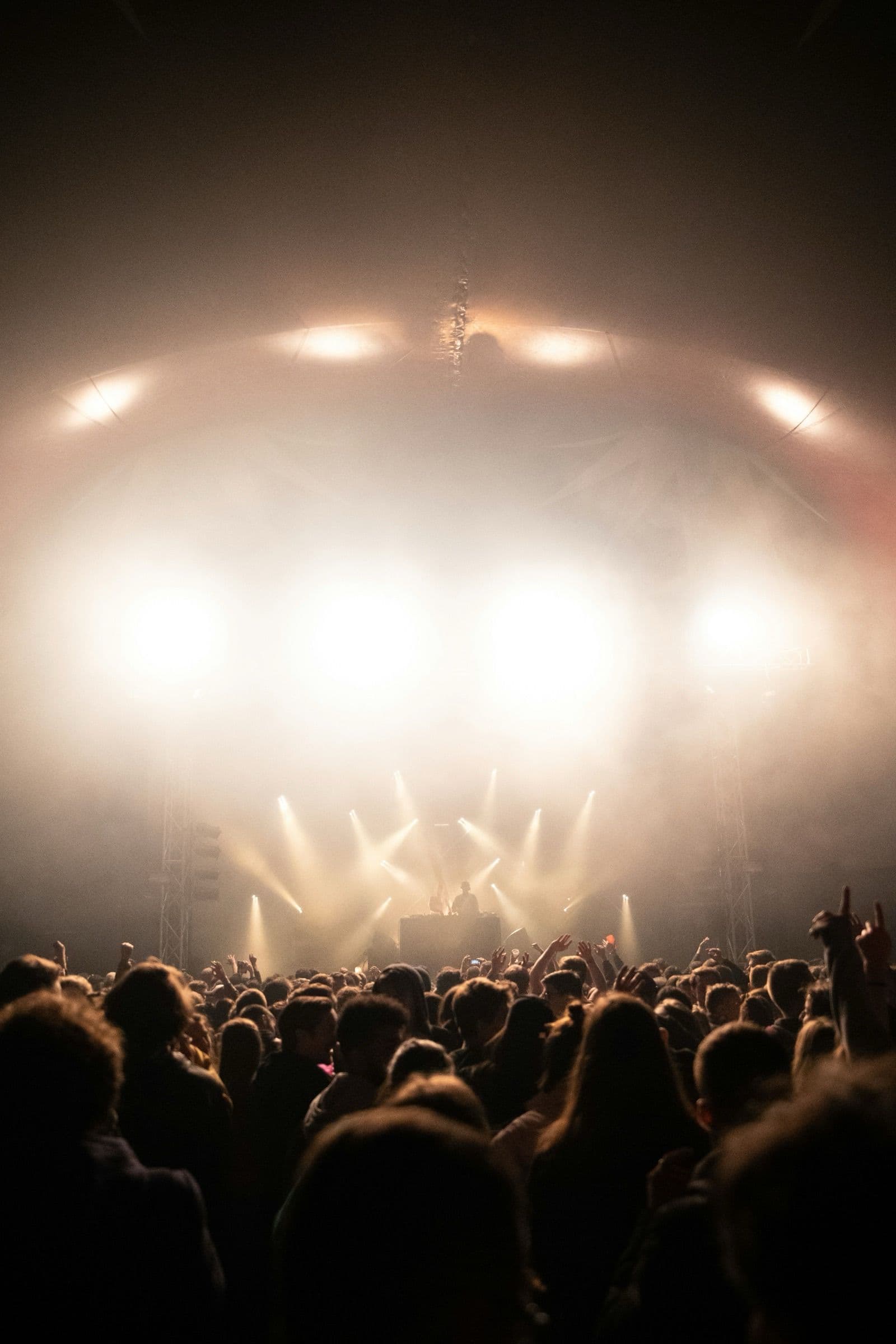 Escenario de festival con focos intensos y el público en silueta delante.